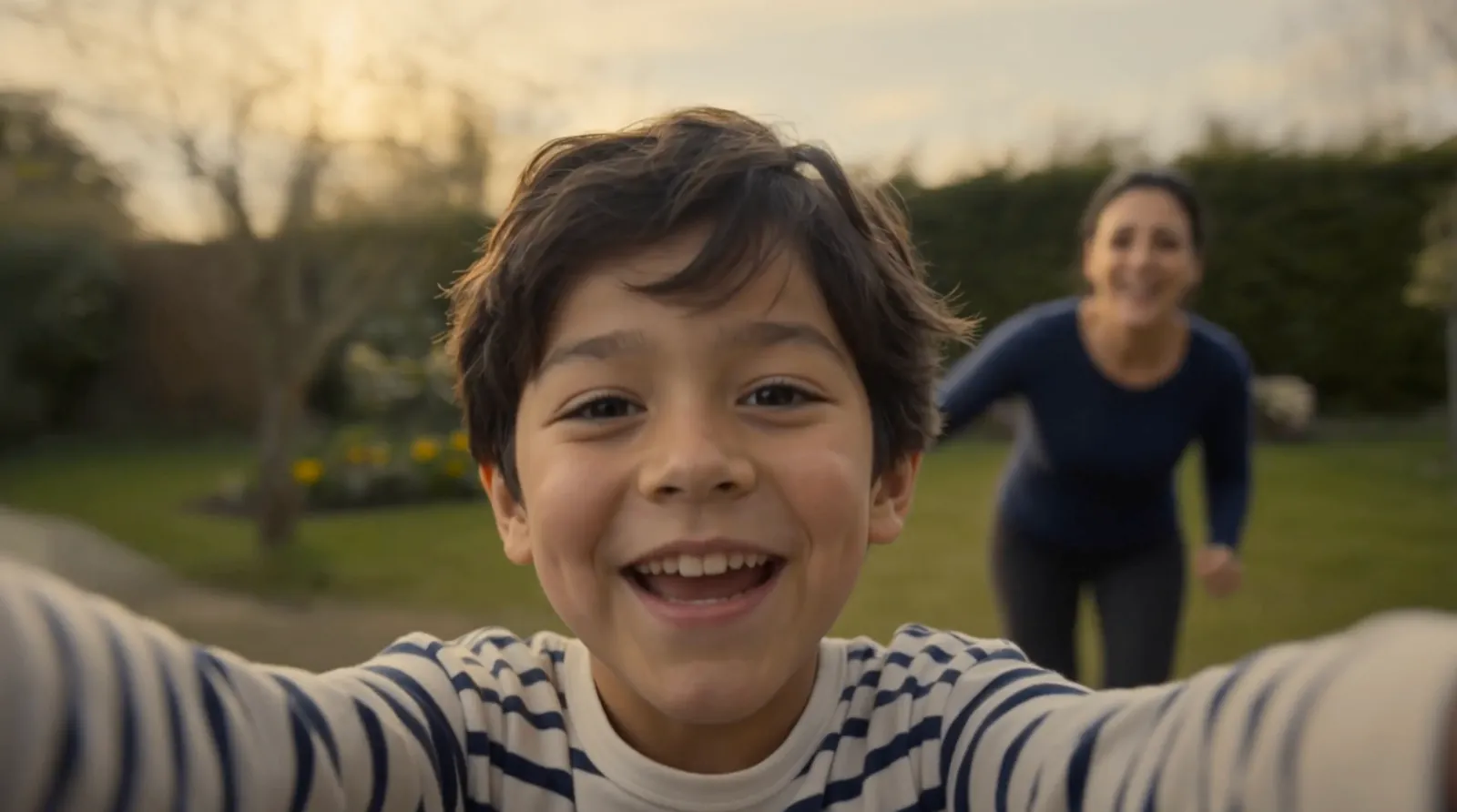Storyboard frame: a boy laughs into the camera as his mother runs behind